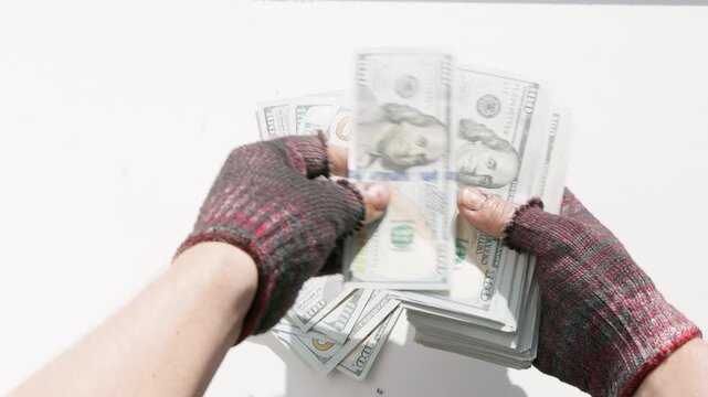 Hands wearing fingerless gloves count a large stack of US dollar bills on a bright white surface. Scene conveys feelings of wealth and financial success.