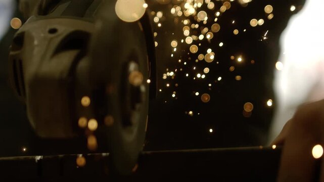 A person is using a grinder to cut metal. Sparks fly from the tool as it touches the metal. The setting is a workshop. The activity is focused and requires skill and care.