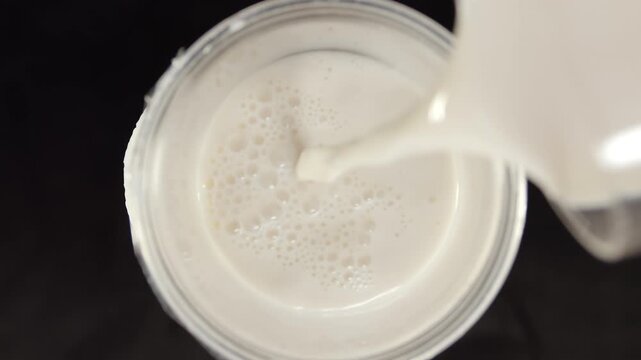 Overhead view of bubble tea with milk flowing into glass and tapioca pearls mixing to form foamy surface patterns