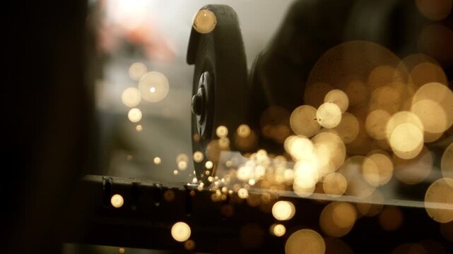 A metalworker uses a grinding tool to shape metal in a workshop. The sparks fly as the tool makes contact, creating bright lights and sounds of work in progress.
