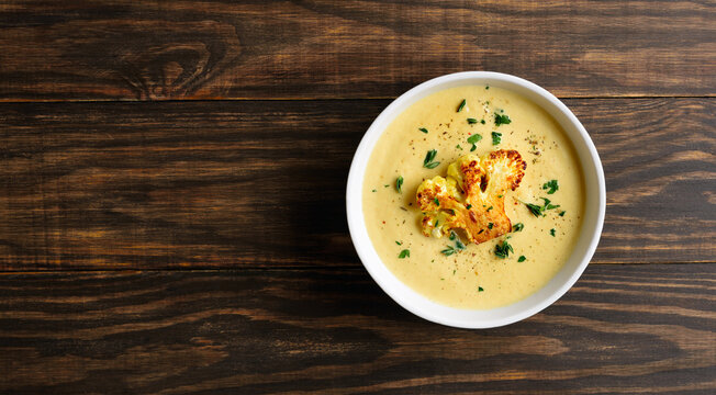 Cauliflower cheese soup in bowl on wooden background with free space
