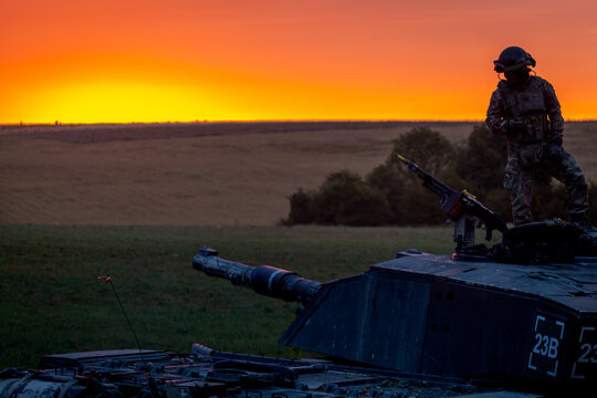 SALISBURY PLAIN, UK - JULY 29, 2025: A British Army Challenger 2 Main Battle Tank silhouetted at sunrise during a military exercise. The tank commander is visible standing in the turret.
