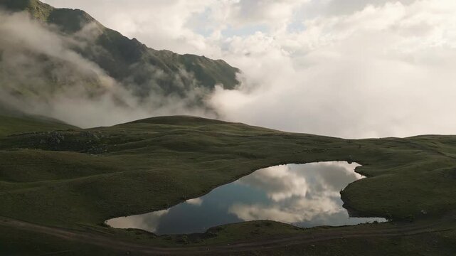 Dramatic morning mist rolling over the Koruldi Lakes in Svaneti, Georgia. A scenic alpine landscape with mountain reflections in the mirror-like water of the Caucasus mountains.