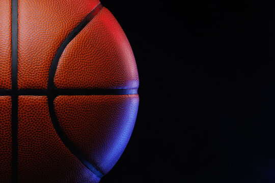 Basketball ball resting against dark background, showing its distinctive pebbled texture and black seams, with vibrant red and blue studio lighting