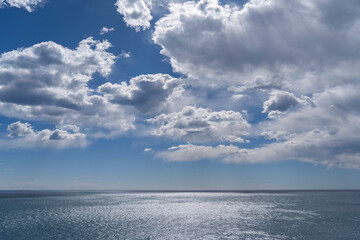 Obraz premium Scenic seascape featuring a shimmering blue ocean under a dramatic sky with fluffy white cumulus clouds and bright sunlight reflecting on the water surface
