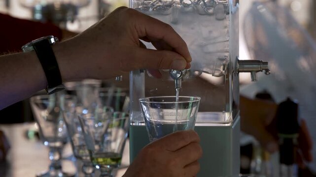 Hand pouring water from absinthe fountain into glass