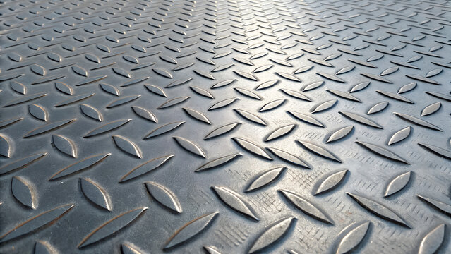 Closeup view of a textured metal diamond plate surface with raised teardrop patterns creating a strong industrial background or floor