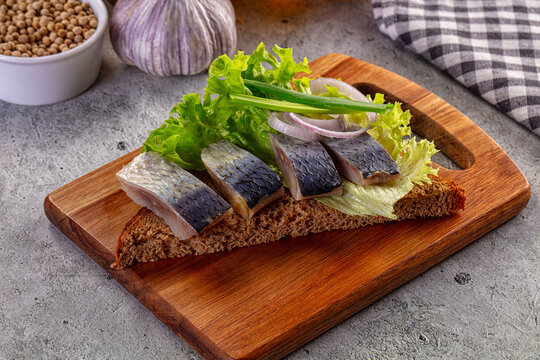 Salted herring appetizer on dark rye bread with lettuce and onions on a wooden board
