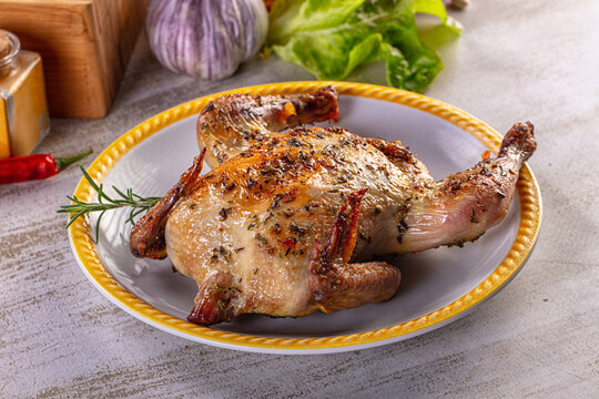 Gourmet roasted whole quail seasoned with herbs on a rustic kitchen table.