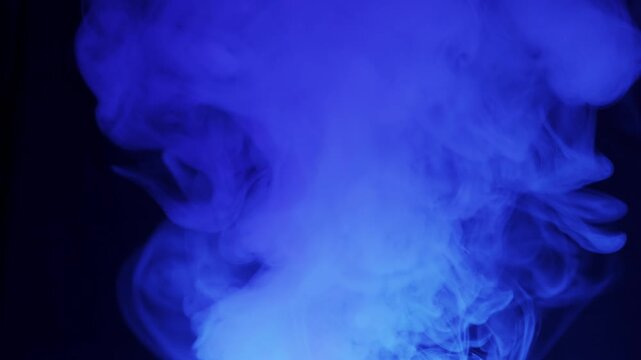 Blue smoke rises and expands, swirling in intricate patterns against a solid black background. Dense vapor is illuminated with a cool blue light, creating an ethereal and atmospheric mood.