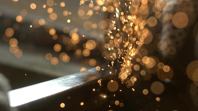 In a workshop, a person is using a tool to shape metal. Sparks fly as the metal is worked on. The focus is on the intense activity and bright sparks from the tool.