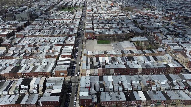 Schoolyard central anchor near S 16th St and W Snyder Ave highlights playground pocket within dense rowhome blocks. Bright roof membranes, scattered greenery, crowded neighborhood in Philly, PA