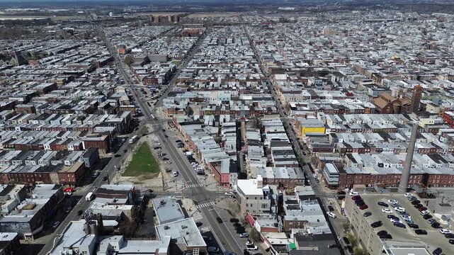 Smokestack district view near S 10th St and Oregon Ave highlights rowhome grids meeting older industrial landmarks. Flat roofs, masonry contrast, soft afternoon haze settle across Philly, PA