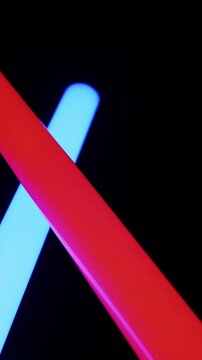 Blue and red neon light swords cross and duel against a solid black background. Bright, vibrant glowing colors create a futuristic and energetic sci-fi aesthetic.