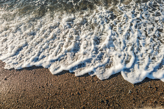 Abstract shoreline with white sea spray in upper third and dark wet sand dominating foreground, minimal coastal texture scene with natural contrast and moody seaside atmosphere