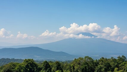 Fototapeta premium A serene mountain landscape with lush green trees under a blue sky