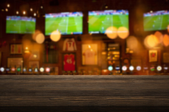 wooden table on foreground and blurred background depicts the lively interior of a sports bar