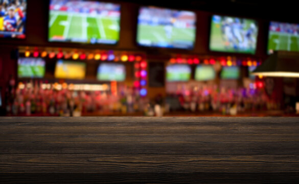 wooden table on foreground and blurred background depicts the lively interior of a sports bar