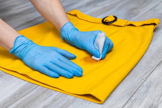 A woman's hand holds a stain remover to remove a dirty spot from a skirt. A greasy stain on a yellow skirt. 