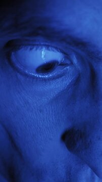 Extreme macro shot reveals male eye darting nervously under monochrome blue light. High detail skin texture and blinking eyelashes convey paranoia or anxiety.