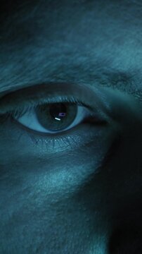 Human eye blinks in extreme close-up showing detailed hazel iris and eyelashes. Cool blue light reflects in the pupil suggesting screen watching or cyber theme.