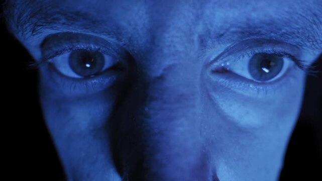 An extreme close-up of a man terrified and wide-open eyes darting back and forth in a dark room. concept of fear, paranoia, insanity, anxiety, and horror.