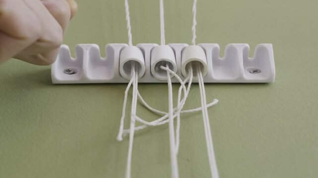 A person hand pulls the cords of a wall-mounted plastic clothes drying rack mechanism installed on a green wall. Concept of household chores, laundry organization, and home maintenance.
