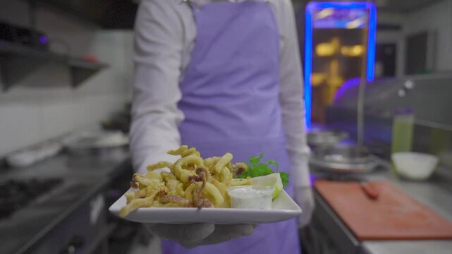 Chef serving crispy fried calamari rings with sauce in restaurant kitchen
