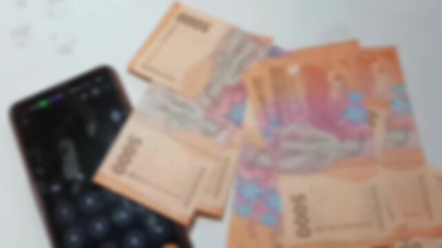 Blurred Indonesian money. Indonesian currency with denominations of 5,000, 10,000, and 20,000 rupiah. Indonesian banknotes are counted using a smartphone calculator isolated on a white background.