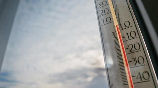 Outdoor thermometer shows red level falling rapidly below zero as clouds rush by during a cold winter evening. Concept of freezing weather, global climate, and meteorology.