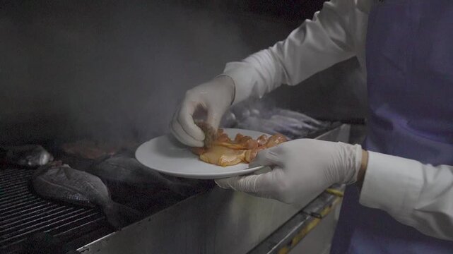 Chef grilling fresh sea bream and serving fish on plate in restaurant kitchen