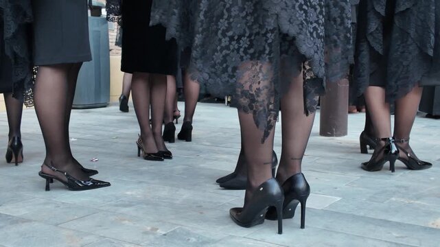 Elegant women wearing black lace mantilla dresses and high heels standing together during Spanish Semana Santa Holy Week traditional Catholic procession street celebration