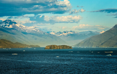 Majestic Alaskan fjord landscape with floating ice, forested island and towering mountains