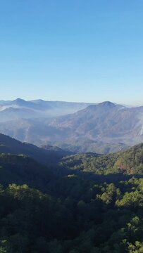 Scenic view of lush green mountains and valleys under a clear blue sky near Bontoc and Sagada in the Philippines. Mist gently settles over the distant hills, creating a tranquil natural atmosphere.