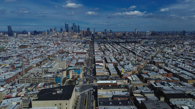 Mid rise district framing near Broad St and Washington Ave shows layered commercial, residential blocks guiding sightlines toward Center City. Flat roofs, parking decks, cloud diffusion Philly, PA