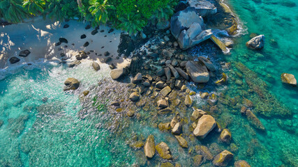 erial drone view of Tusculum Beach in Mahé, Seychelles, showcasing pristine white sand framed by striking granite boulders. Crystal-clear turquoise waters gently meet the shore © Nils