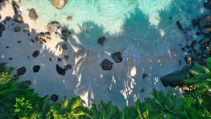 erial drone view of Tusculum Beach in Mahé, Seychelles, showcasing pristine white sand framed by striking granite boulders. Crystal-clear turquoise waters gently meet the shore © Nils