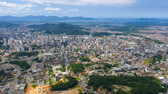 Wide aerial view of Joinville showing urban expansion, green hills and Babitonga Bay, Santa Catarina.