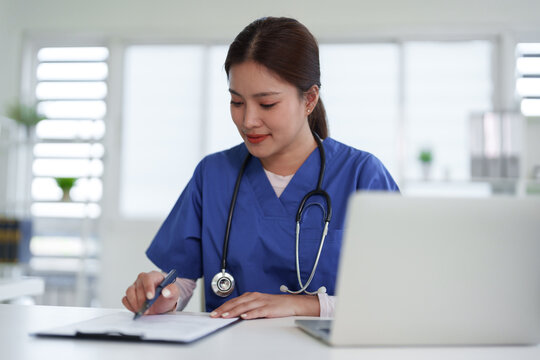 Asian Adult Female Doctor Nurse Healthcare Professional Writing Medical Document Patient Report Clipboard Laptop Desk Office Clinic Hospital