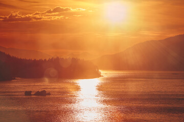 Golden Alaskan fjord sunset illuminating calm waters and distant forested mountain silhouettes
