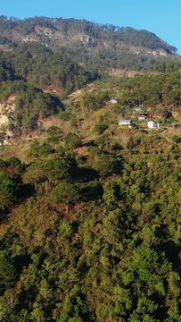 Aerial view of a lush green mountain landscape with scattered houses nestled among trees in Bontoc, Philippines. The scene captures the natural beauty and rural tranquility of the region.