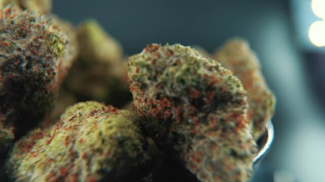 Close up cinematic rotating motion shot of many green and orange cannabis buds in a bowl, showing intricate textures and vibrant colors of the marijuana