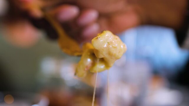 Close up slow motion footage of a person scooping cheesy mac and cheese with a golden fork from a white bowl, showing cheese pulls