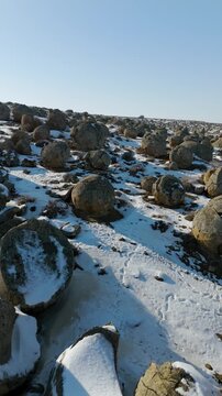 Vertical close-up drone footage of spherical stone concretions in the Torysh Valley. The winter landscape of Mangystau highlights the texture of the snow-covered remains of the ancient Tethys Ocean. A