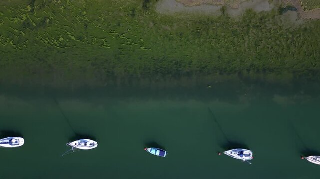 Top down aerial view of sailing boats mooring in nature reserve. Beautiful algae abstract patterns in the water. Shades of green and blue water. in salty marsh. Peaceful background scene.