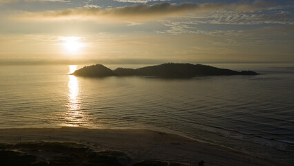 Fototapeta premium Aerial view of Campeche Island silhouette at sunrise with golden light reflecting on calm sea, Florianopolis.