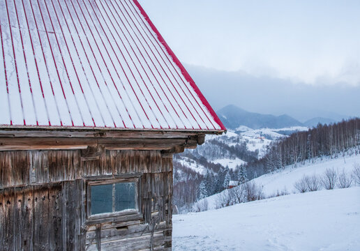 Rustic wooden cabin with snow-covered roof overlooking winter mountains and forest landscape