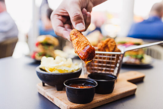 Hand dipping a crispy chicken nugget into red dipping sauce on rustic wooden serving board