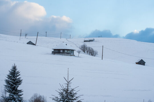 Snowy rural landscape with traditional wooden houses on winter hills under cloudy sky