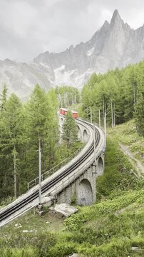 The iconic red train crossing a stone viaduct in the French Alps near Chamonix, scenic mountain landscape.